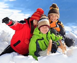 3 freudige Personen auf einer Rodel im Schnee